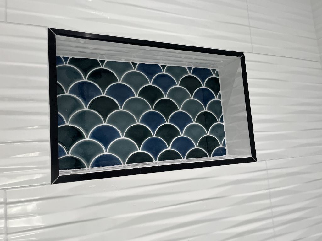 Shower niche with blue scallop mosaic tile accent and black trim